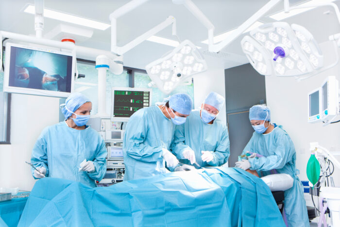Four surgeons in an operating room with a display screen behind them.
